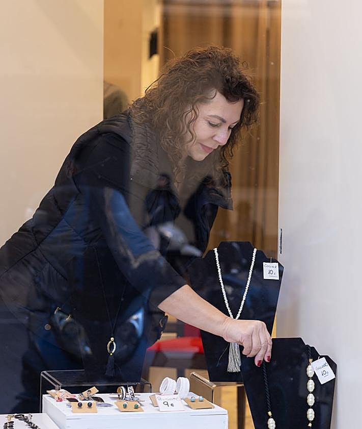 Imagen secundaria 2 - Dos detalles del stock de la tienda y Natalia colocando un collar en el escaparate.